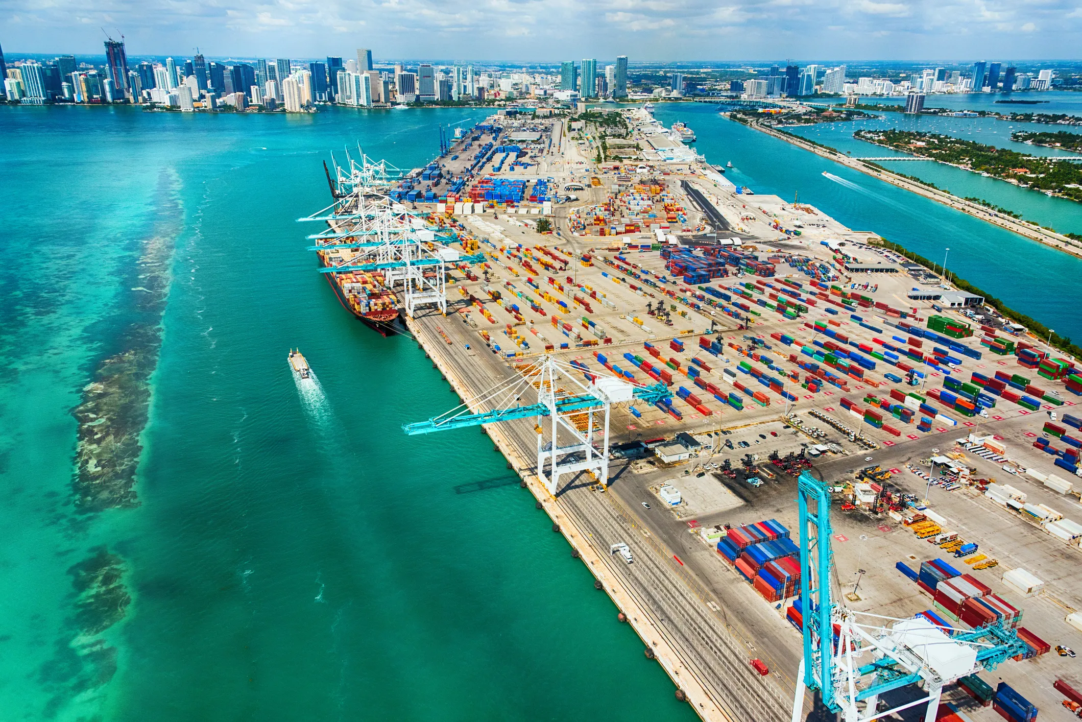 Aerial view of PortMiami cargo terminal showing container ships at dock, stacks of shipping containers across the cargo yard, and the Atlantic shipping channel — the multimodal cargo gateway nearest the miamidade3pl Pompano Beach operations.