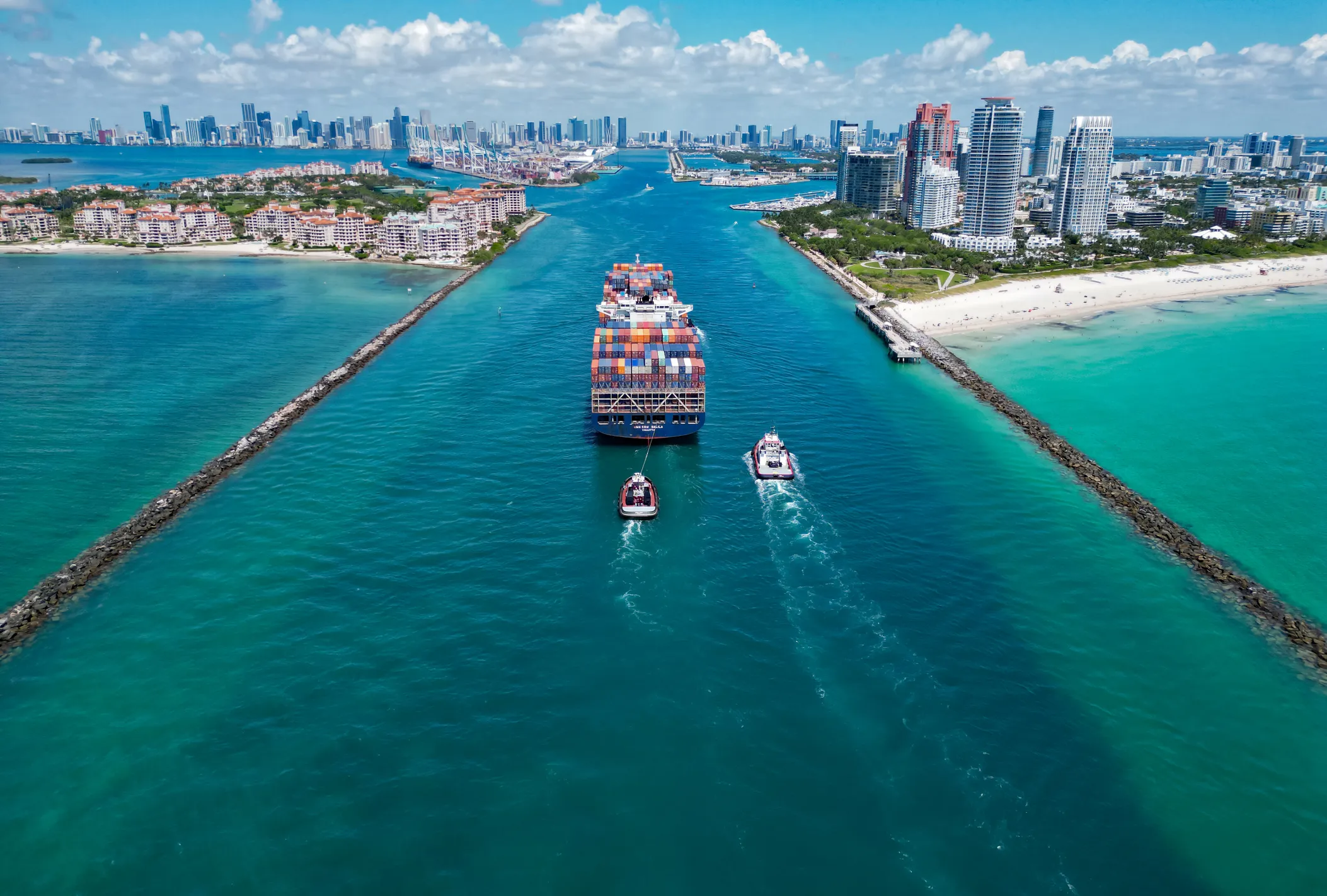 Aerial view of PortMiami on Dodge Island in Biscayne Bay, showing the cargo container terminals, the post-Panamax channel through Government Cut, and downtown Miami in the background.